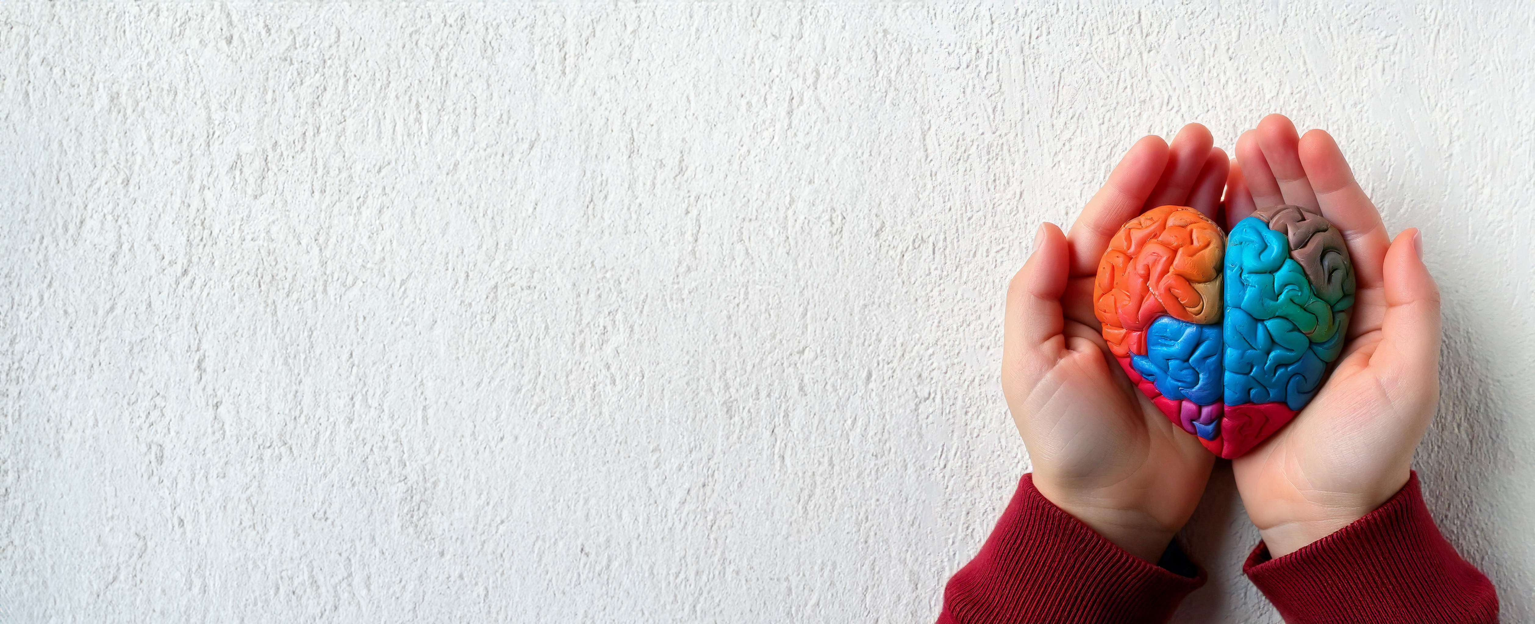 Small child's hand holding colorful heart-shaped brain made of clay or doh.
